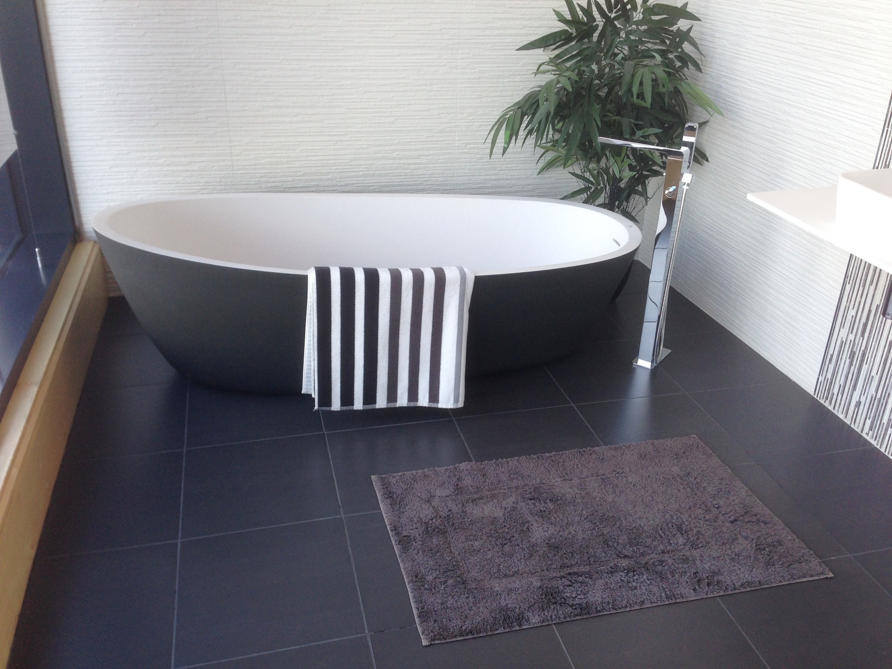 A freestanding bathtub with a towel and floor mat.